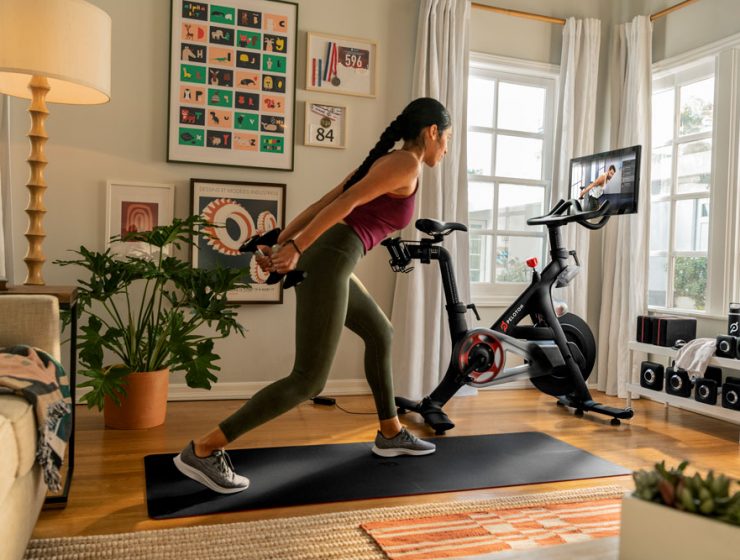 A woman doing dumbbell rows beside her Peloton bike