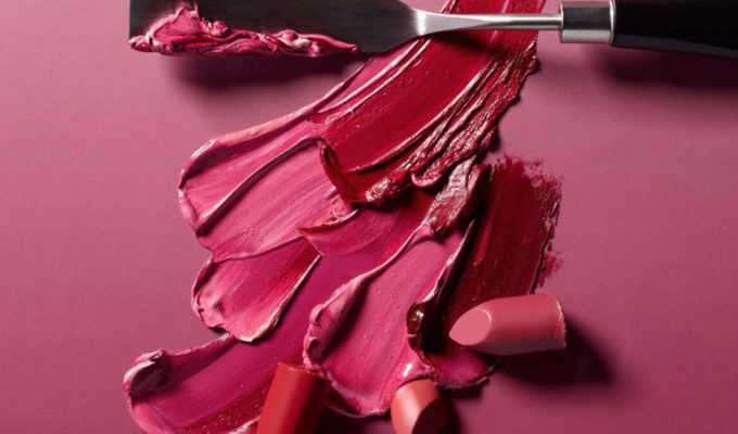 A palette of pinks, orange and red lipsticks swatched with a metal spatula.