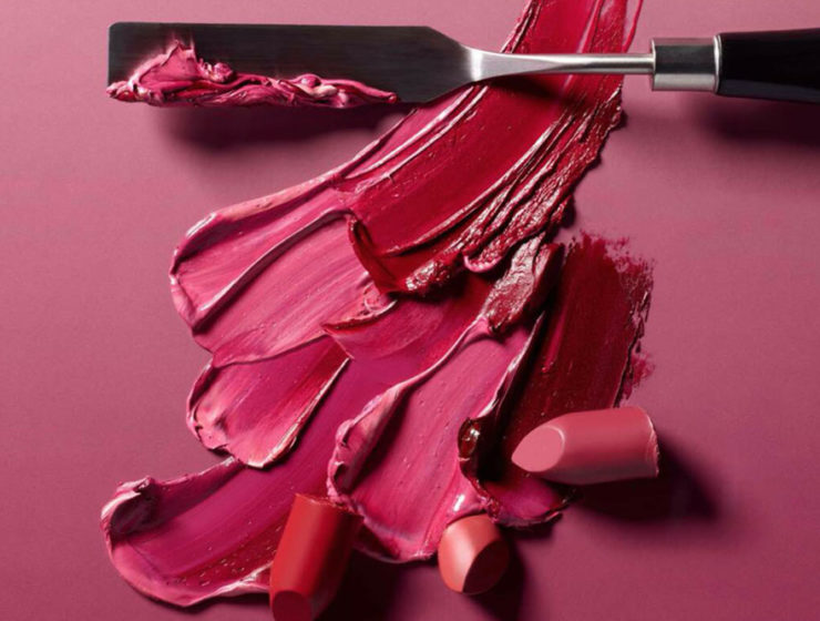 A palette of pinks, orange and red lipsticks swatched with a metal spatula.