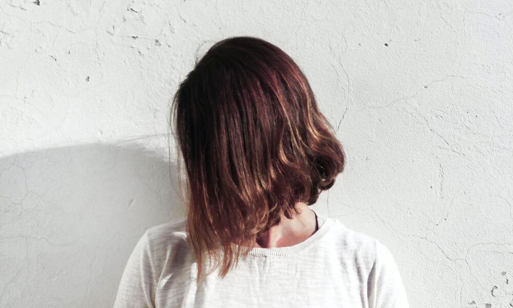 woman with damaged hair in lockdown stands with hair in face against wall