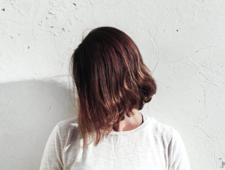 woman with damaged hair in lockdown stands with hair in face against wall