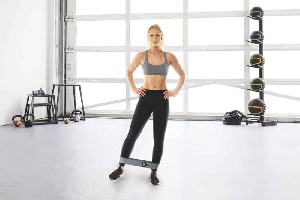 A woman doing standing leg lifts using the Everlast Woven Resistance Band