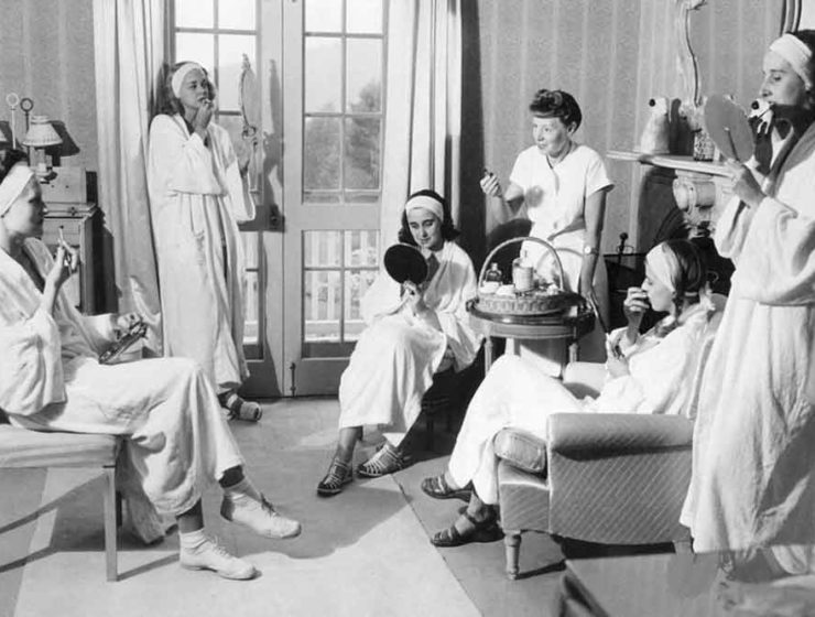 A vintage photo of women at the Elizabeth Arden spa in 1952, lounging and looking at themselves in mirrors as they apply lipstick