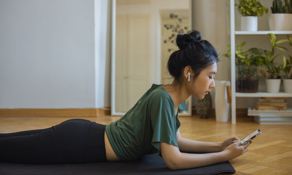 A woman starting her workout on the floor in her living room, as she sets up her phone.