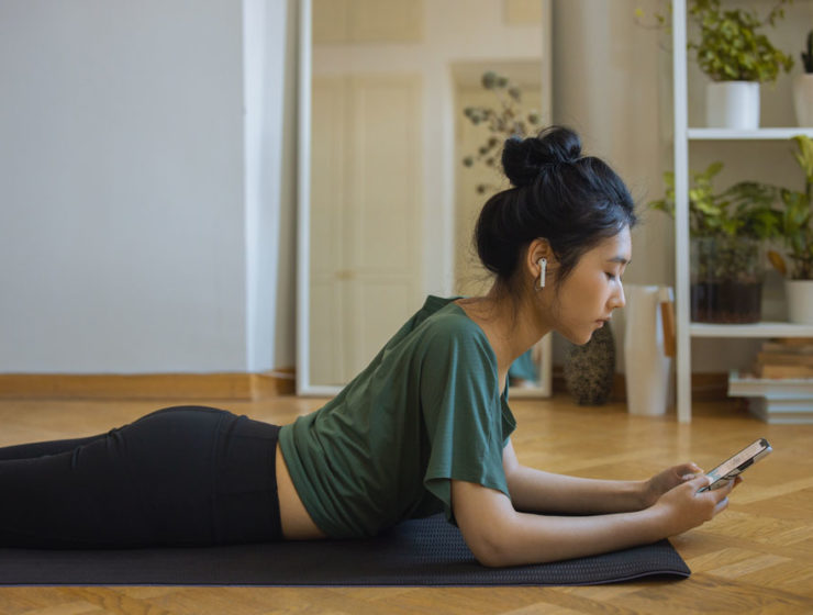 A woman starting her workout on the floor in her living room, as she sets up her phone.