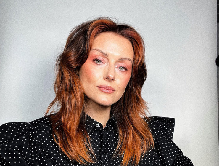 Makeup artist Katie Jane Hughes is on set with a paper backdrop behind her.