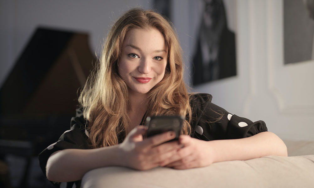 A woman in a polka-dot blouse glancing up from her cellphone to smile