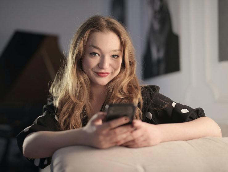 A woman in a polka-dot blouse glancing up from her cellphone to smile