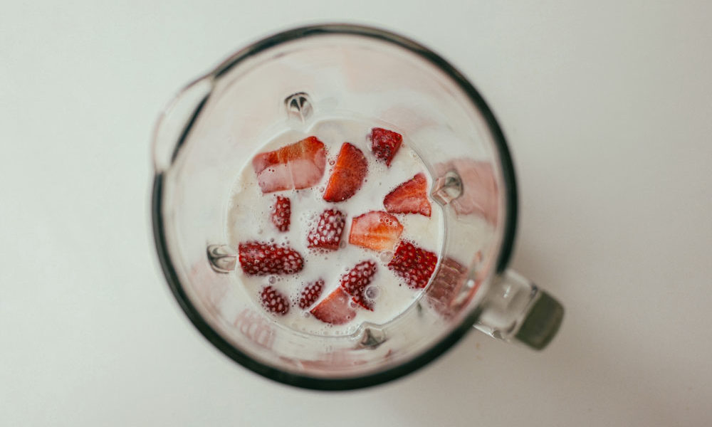 A blender filled with a dairy-alt drink and loads of strawberries