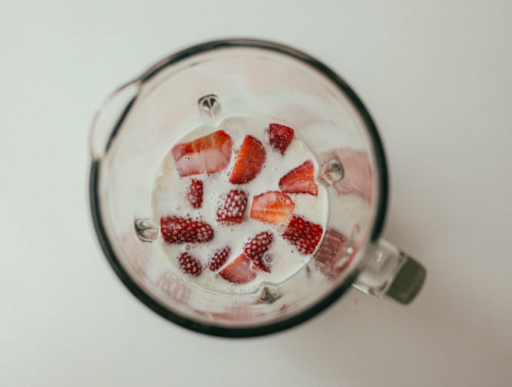 A blender filled with a dairy-alt drink and loads of strawberries