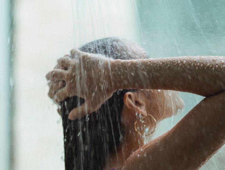 A woman enjoying a shower, with her hands above her head and large droplets of water on her hair, hands and arms