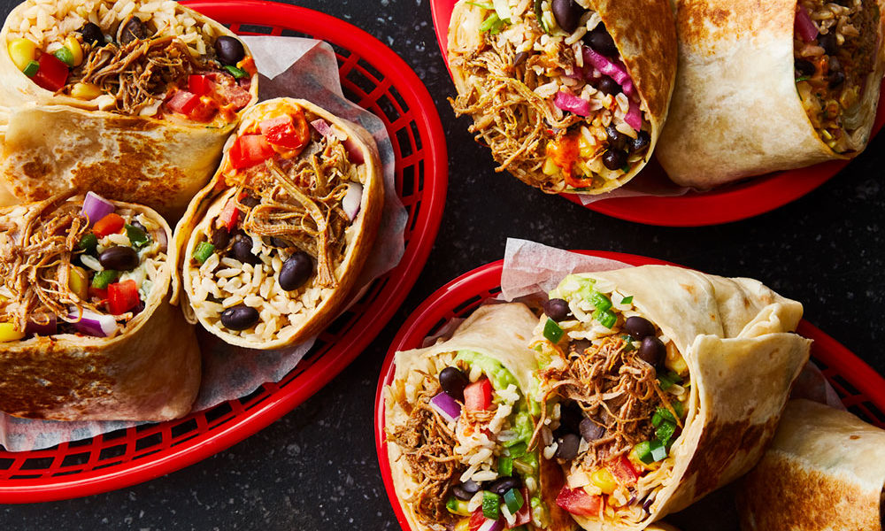 Three baskets of burritos cut in half, with the spicy chicken spilling out of the tortillas
