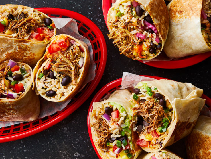 Three baskets of burritos cut in half, with the spicy chicken spilling out of the tortillas