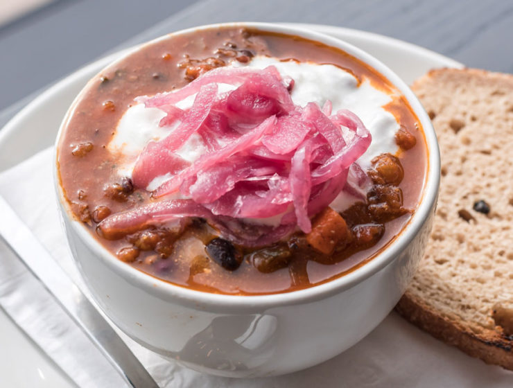 A hearty bowl of turkey chili loaded with beans and topped with pickled onions, served with a piece of rye bread.