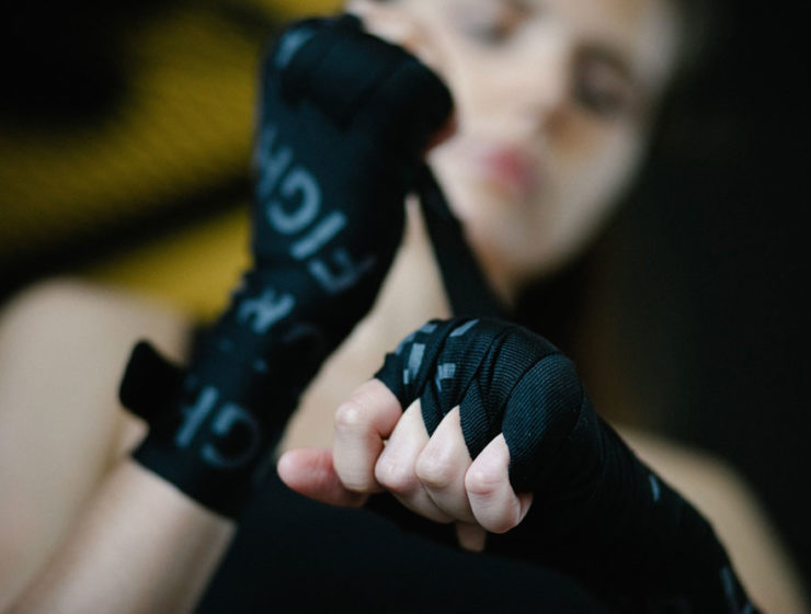 A woman is prepping her hands for a shadow boxing sesh with boxing wraps