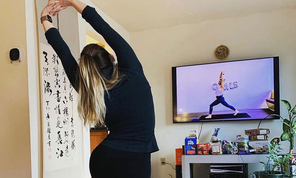 A woman is in warrior pose while watching Kardia instructor Heather in the same pose