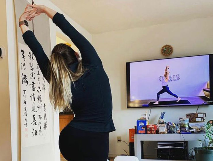 A woman is in warrior pose while watching Kardia instructor Heather in the same pose