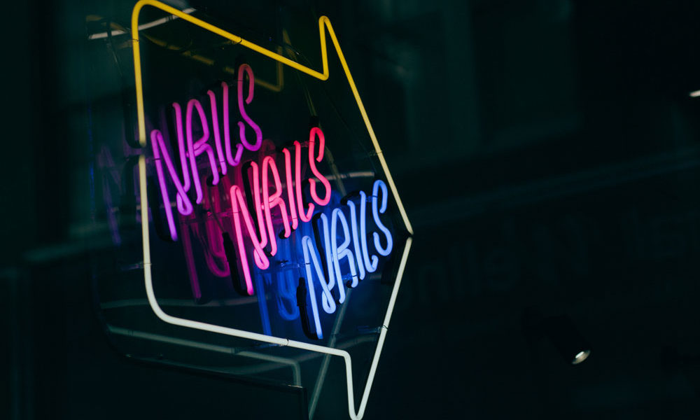 A neon bright sign with the words "nails, nails, nails" in bright colours against a dark cook background