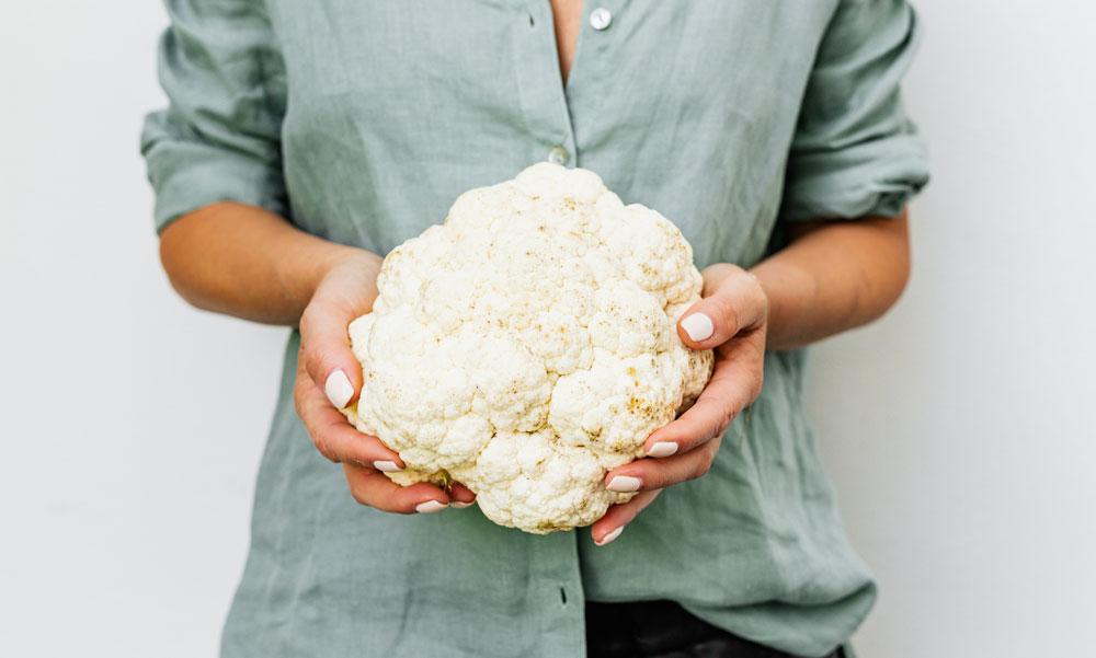 Woman holds a head of cauliflower, ready for David Rocco's Cauliflower Putannesca recipe