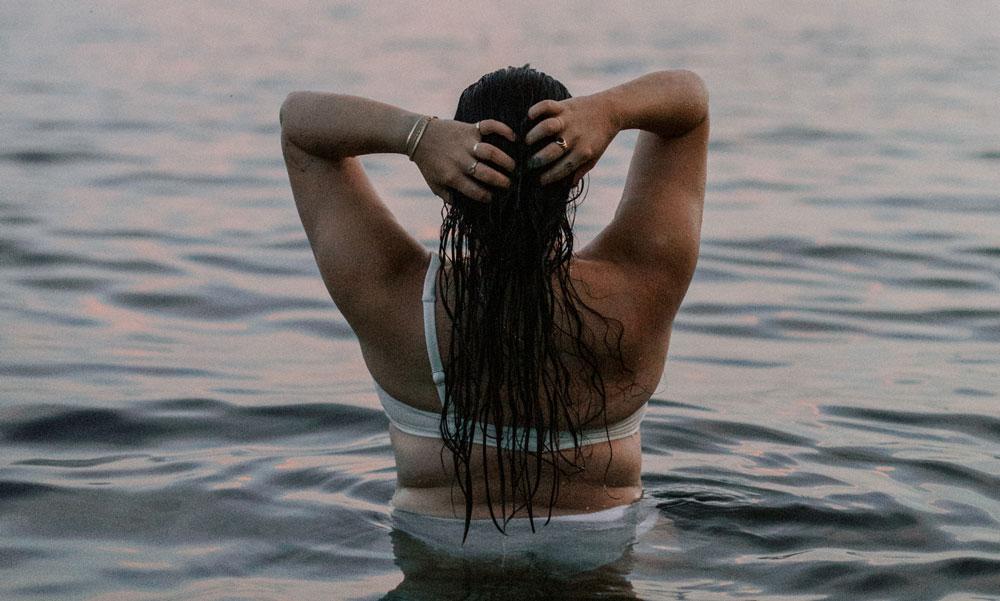 Woman in the ocean, staring out, wanting to keep that summer feeling all year long.